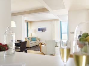A modern hotel room with a sofa, armchairs, a dining table, and a view of the outdoors.