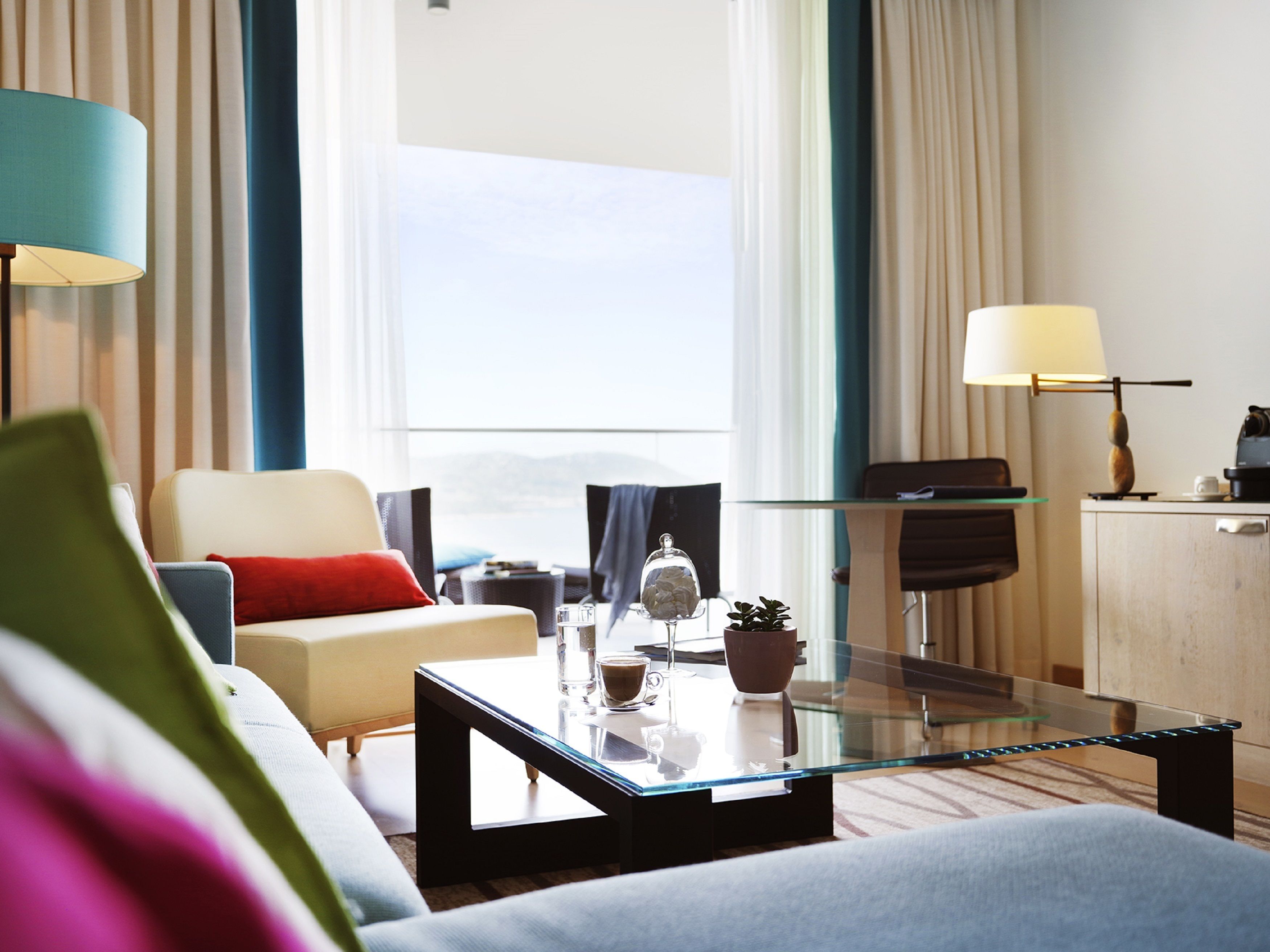 Een moderne hotelkamer met een glazen salontafel, een bank, een fauteuil en uitzicht op de omgeving.