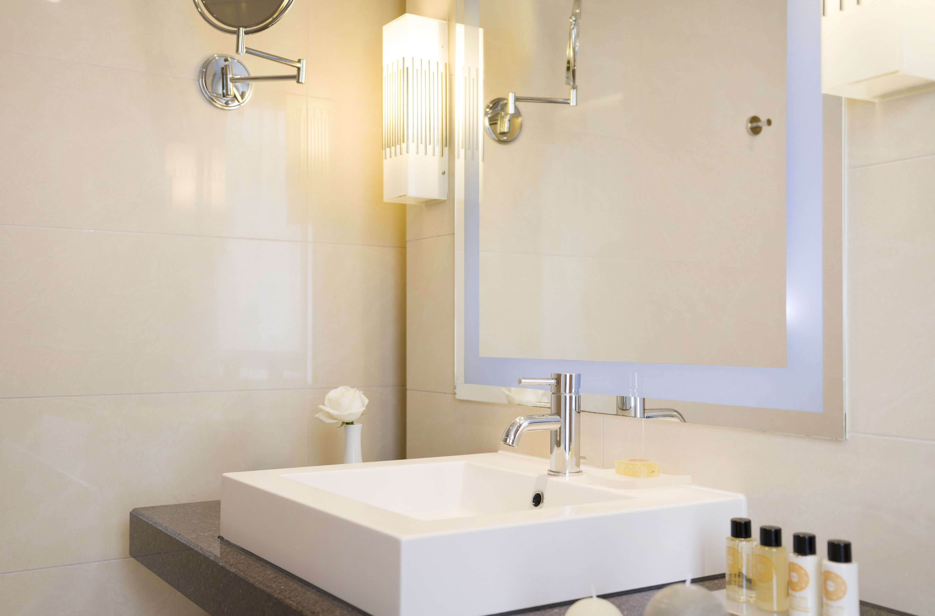 A modern bathroom with a large mirror, a white sink, and a marble countertop.