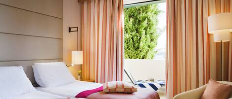 Habitación de hotel con dos camas, una silla, ventana con cortinas y vistas a zonas verdes.