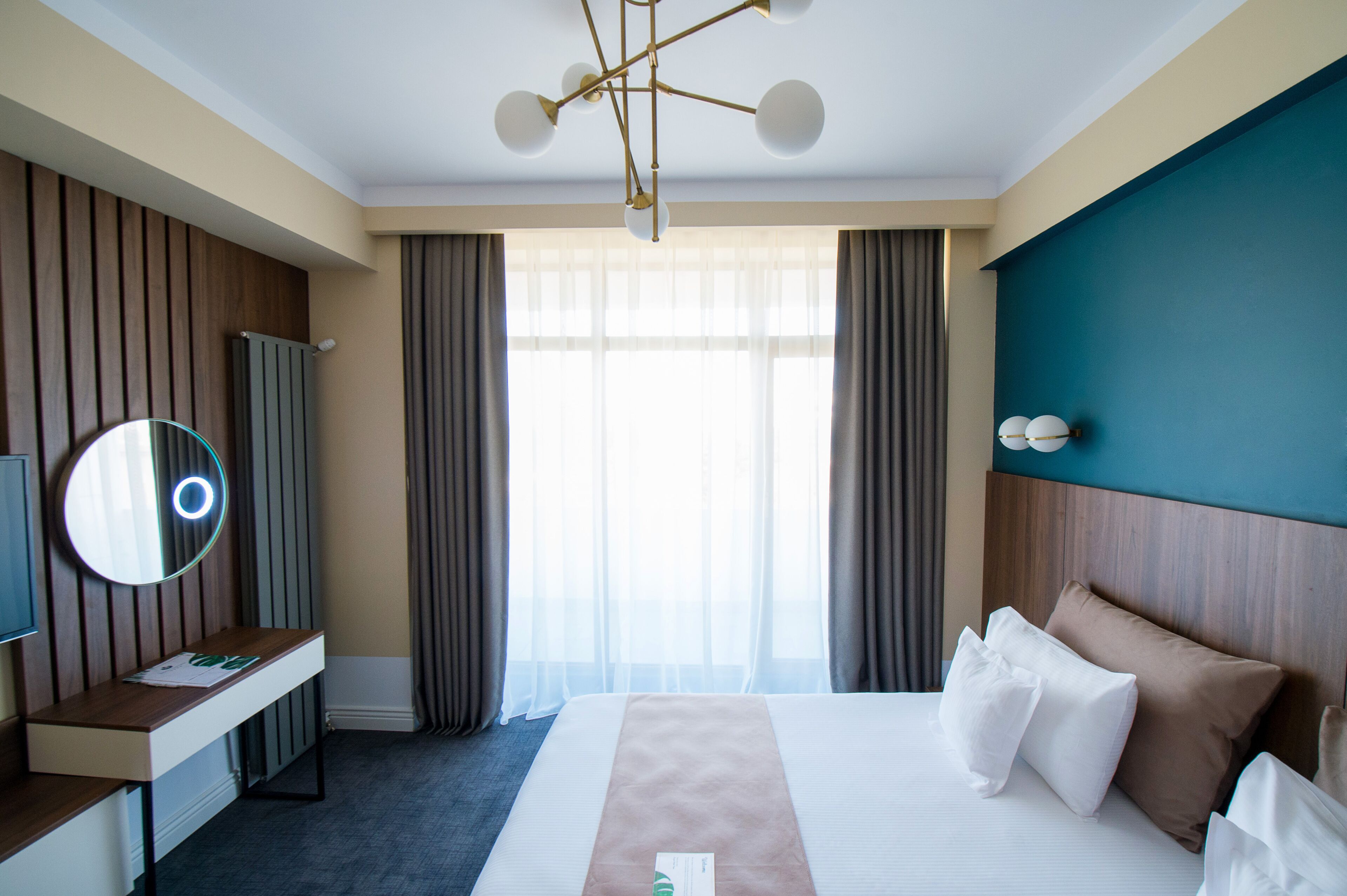 Hotelkamer met een bed, bureau, spiegel, televisie en een raam met gordijnen.