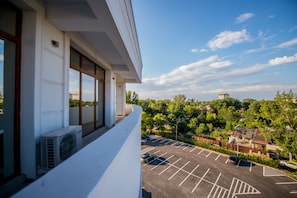 A view from a balcony overlooking a parking lot and a green area with trees and buildings in the distance. - Hotel Oxford (Constanta)