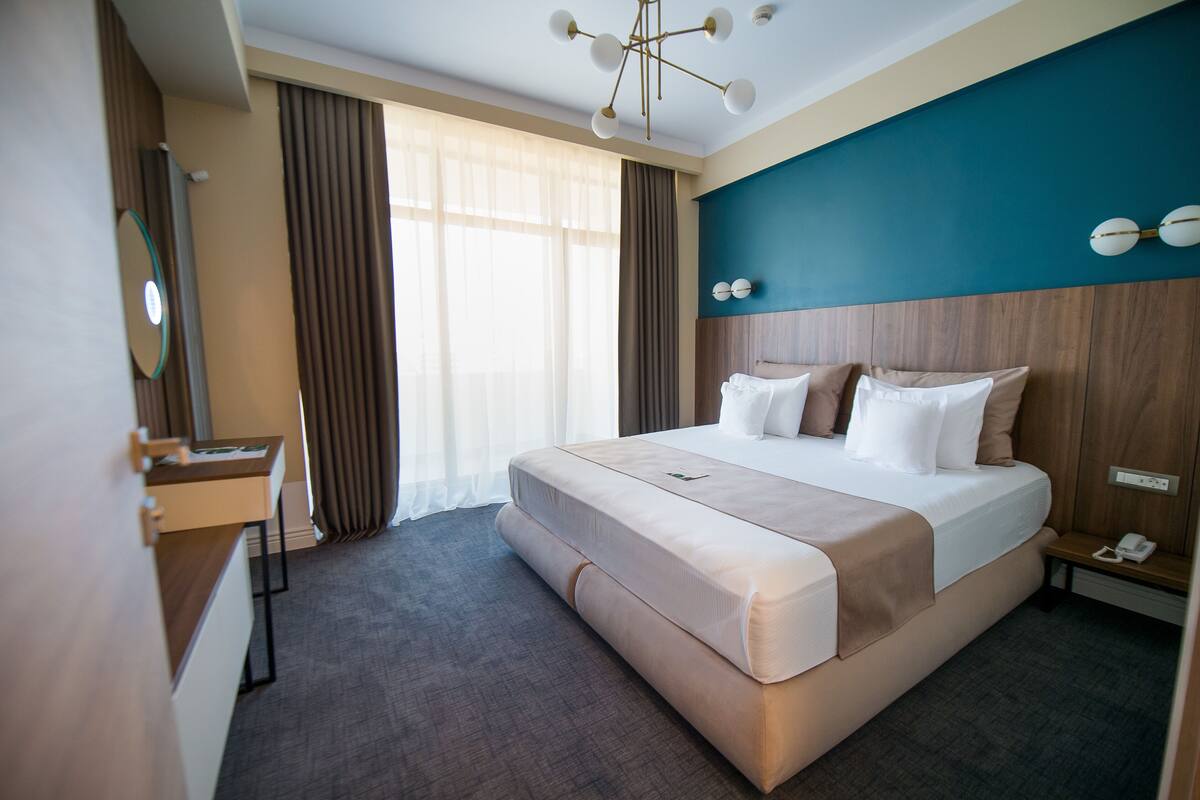 A hotel room with a large bed, a bedside table, a desk, and a mirror.
