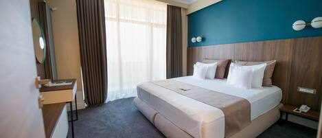 A hotel room with a large bed, a bedside table, a desk, and a mirror.