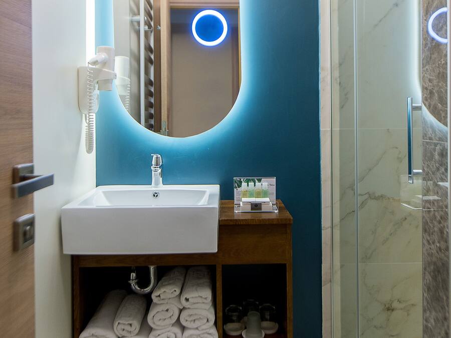 A bathroom with a white sink, a mirror with a blue illuminated frame, and a glass shower enclosure.