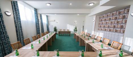 Un salón de conferencias con mesas largas, sillas y botellas verdes.