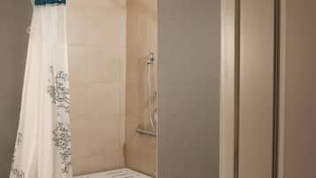 Ducha con cortina blanca, azulejos color beige y cabezal de ducha.