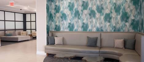 A modern lobby with a grey sectional sofa, two small round tables, and a textured wall with a wave pattern.