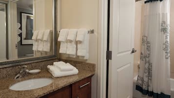 A bathroom with a granite countertop sink, a large mirror, and a shower with a floral curtain.
