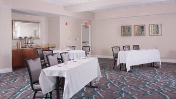 A conference room with two tables, chairs, a mirror, a sink, and a patterned carpet.