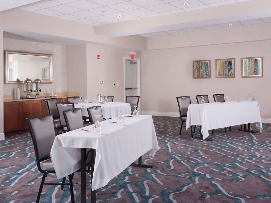 A conference room with two tables, chairs, a mirror, a sink, and a patterned carpet.