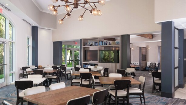 A spacious dining area with multiple tables and chairs, large windows, and a modern chandelier. - Residence Inn by Marriott Fort Myers Sanibel (Fort Myers)