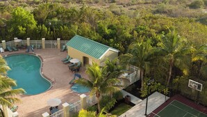 A swimming pool area with lounge chairs, a small building, and a basketball court surrounded by palm trees and greenery. - Residence Inn by Marriott Fort Myers Sanibel (Fort Myers)