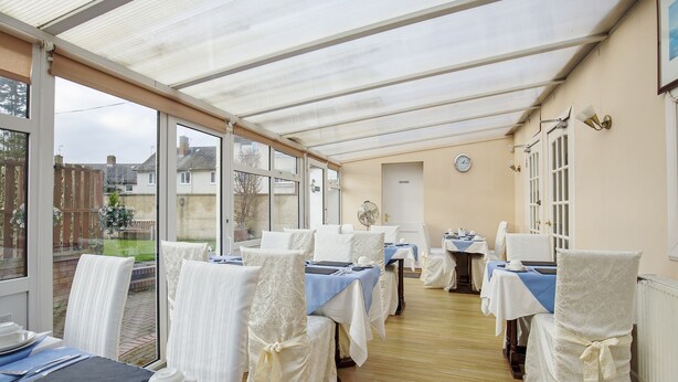A conservatory with tables set for dining, large windows, and a clock on the wall. - Arden Guest House, Craigmillar Castle Edinburgh (Edinburgh)