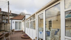 A covered patio area with brick flooring, white walls, and a glass door leading to a room with a bed and a table set for dining. - Arden Guest House, Craigmillar Castle Edinburgh (Edinburgh)
