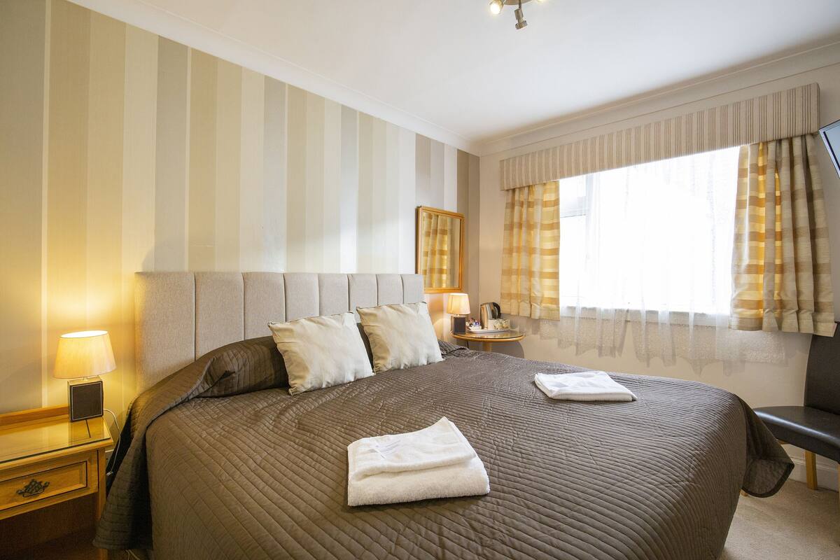 A neatly made bed with pillows, a bedside lamp, and a folded towel on the bed.