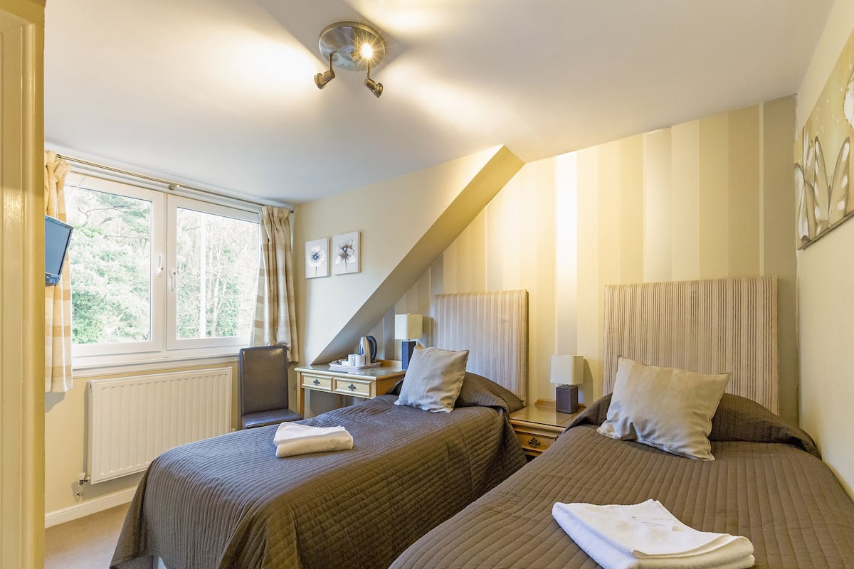 A hotel room with two beds, a desk, a chair, and a window with curtains.