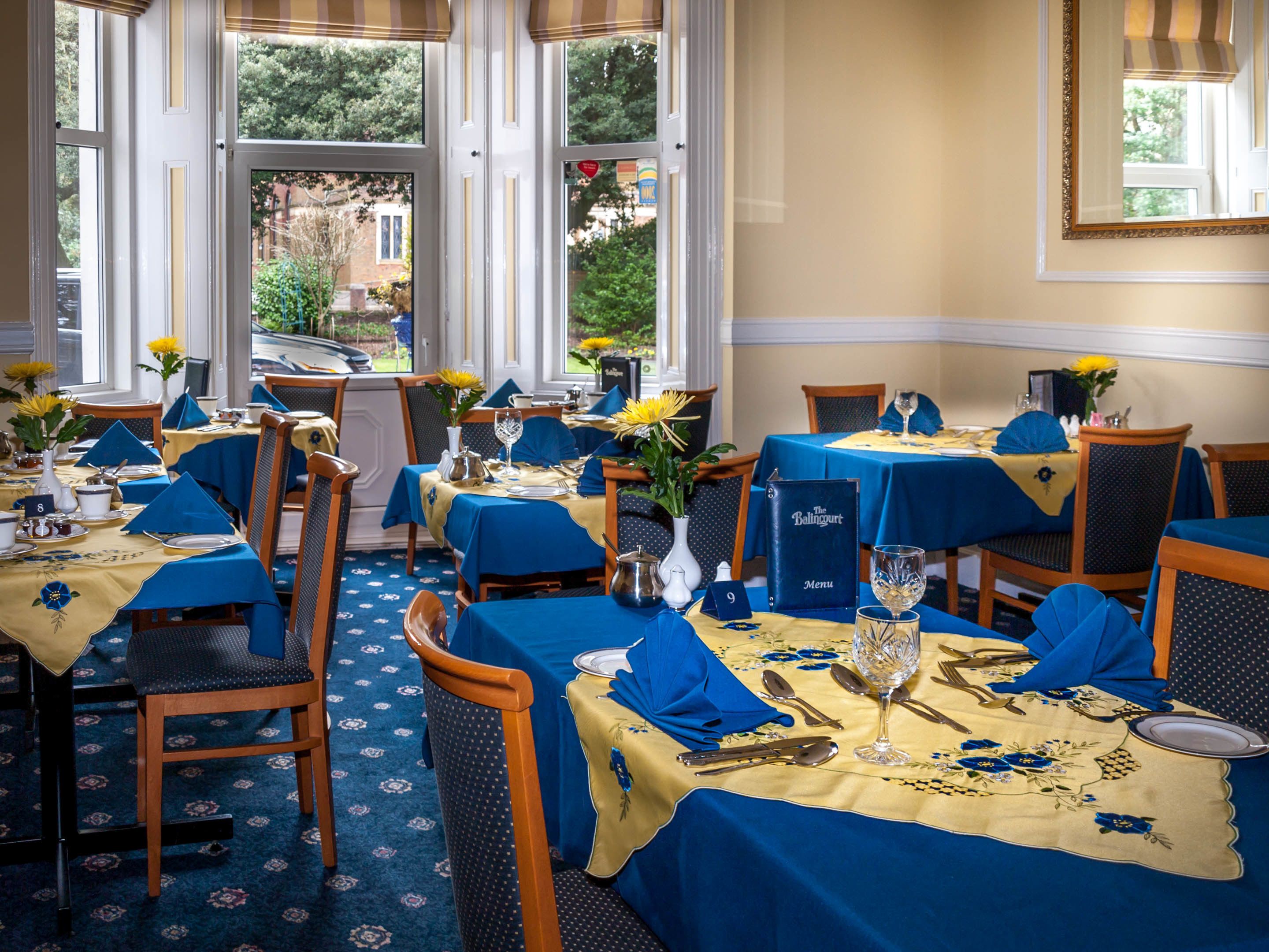 A restaurant with tables set for dining, featuring blue tablecloths and chairs, and a menu stand.