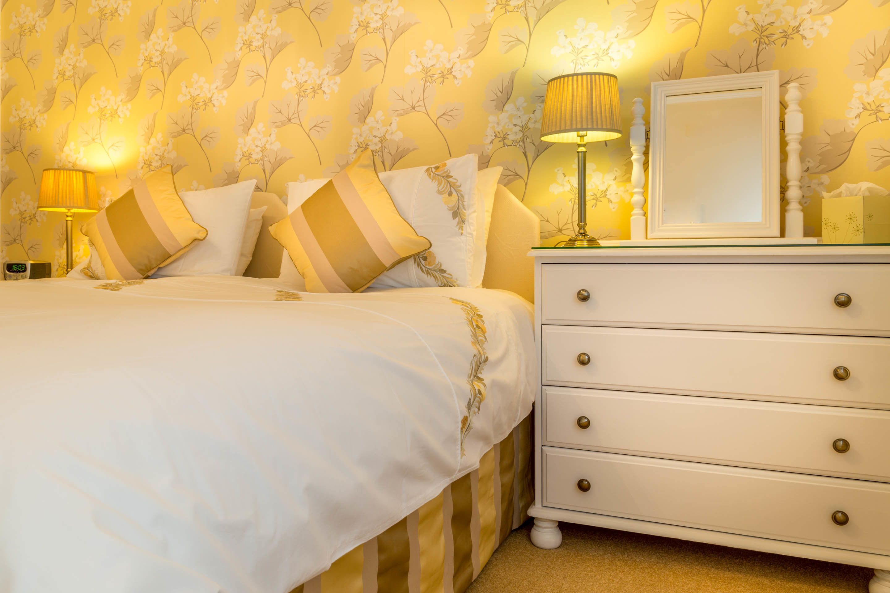 A neatly made bed with striped bedding, a bedside lamp, and a dresser with drawers.