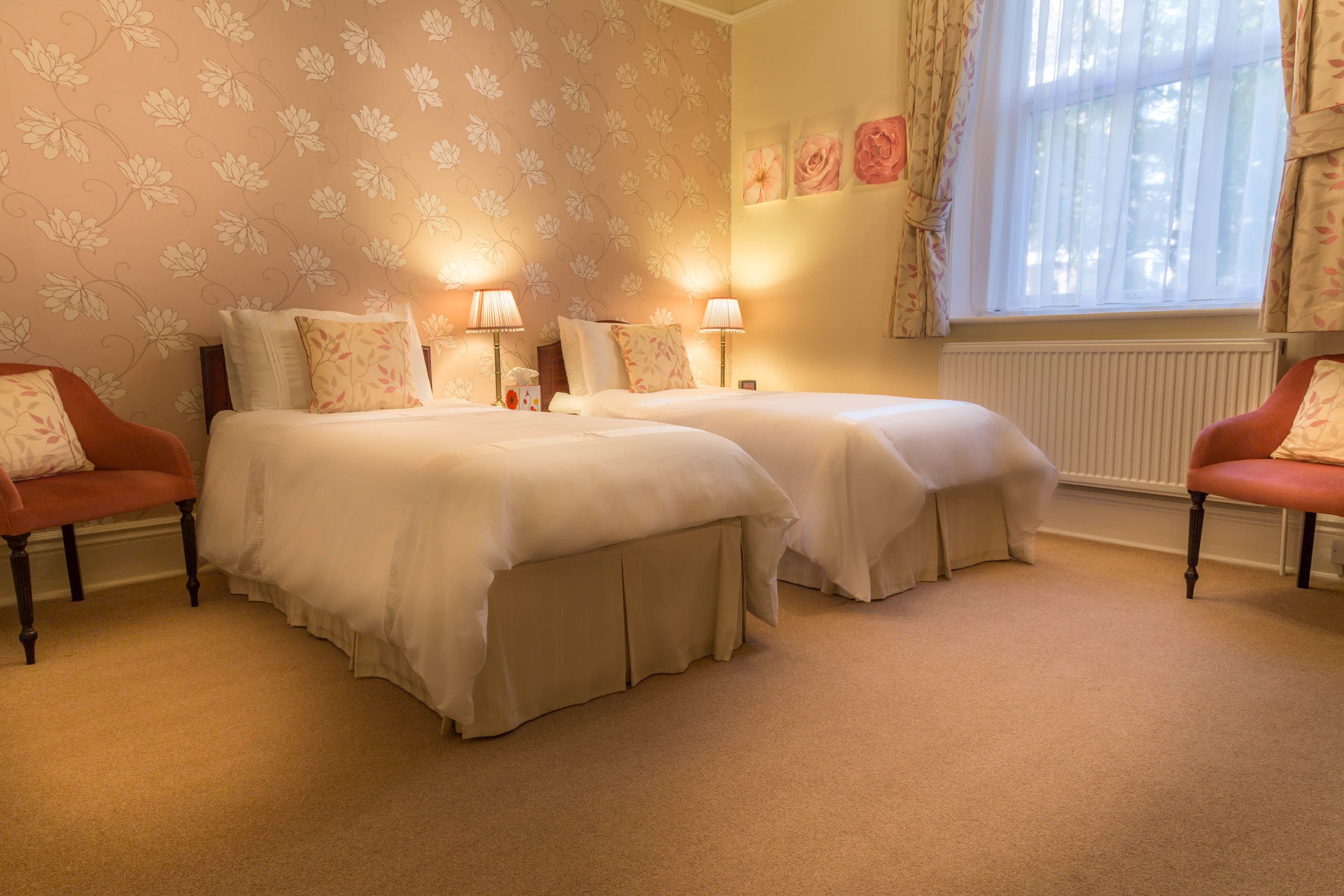 A hotel room with two beds, a window with curtains, and a radiator.