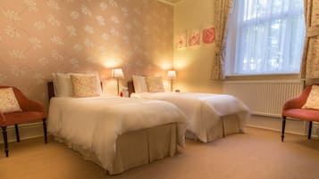 A hotel room with two beds, a window with curtains, and a radiator.