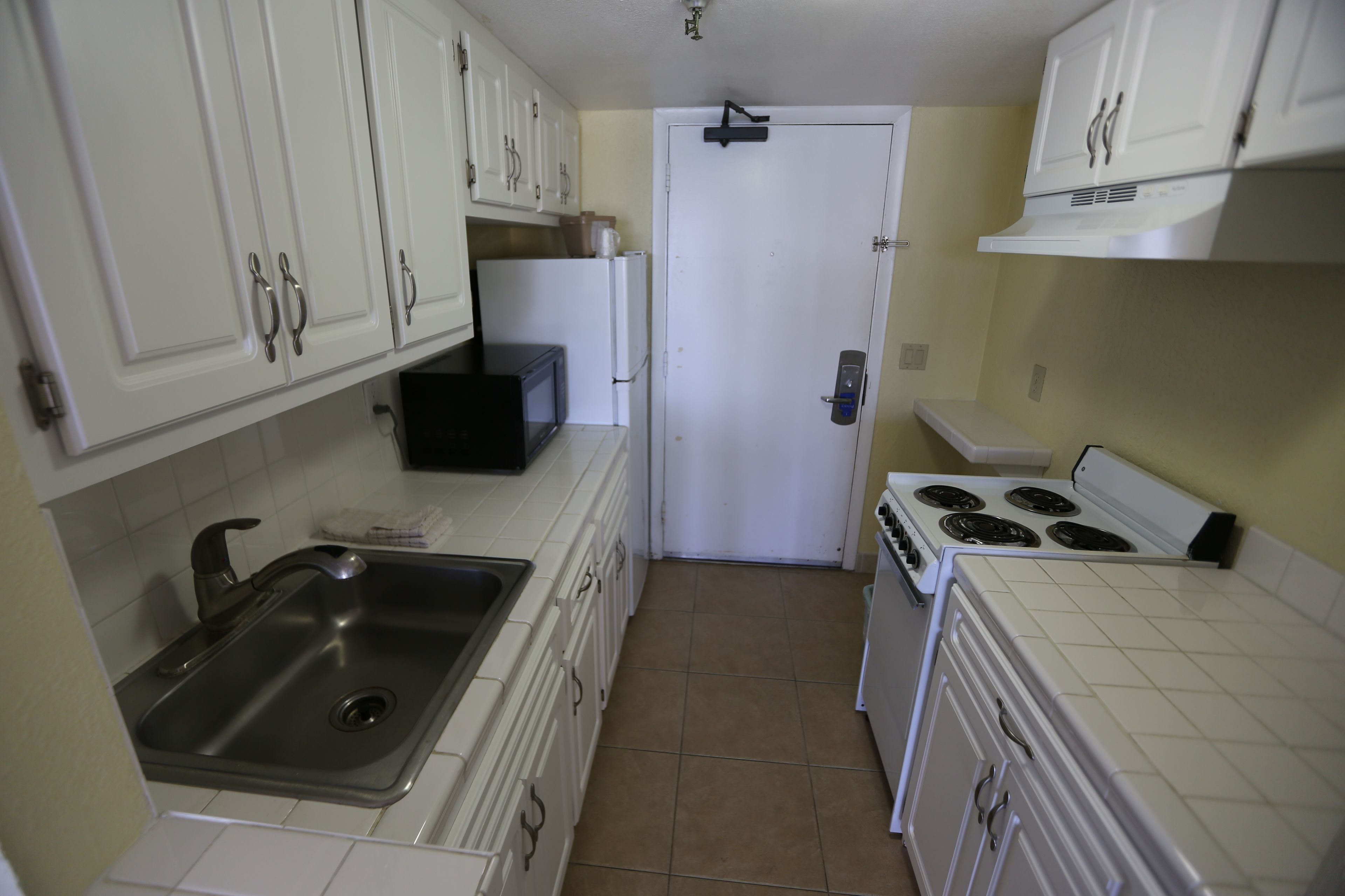 Una cocina compacta con armarios blancos, un lavamanos de acero inoxidable, un microondas y una estufa.
