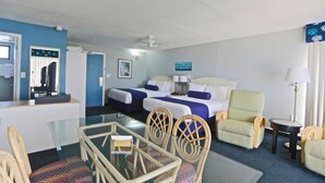 Une chambre d’hôtel avec un lit, deux chaises, une table, une lampe et un ventilateur de plafond.
