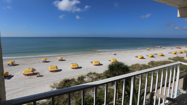Une vue sur la plage depuis un balcon, avec des parasols jaunes et des chaises longues.