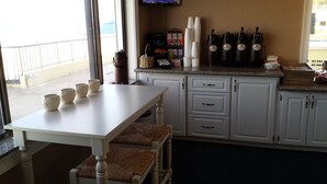 Une cuisine avec un plan de travail blanc, une table à manger avec quatre chaises et une fenêtre donnant sur un immeuble.