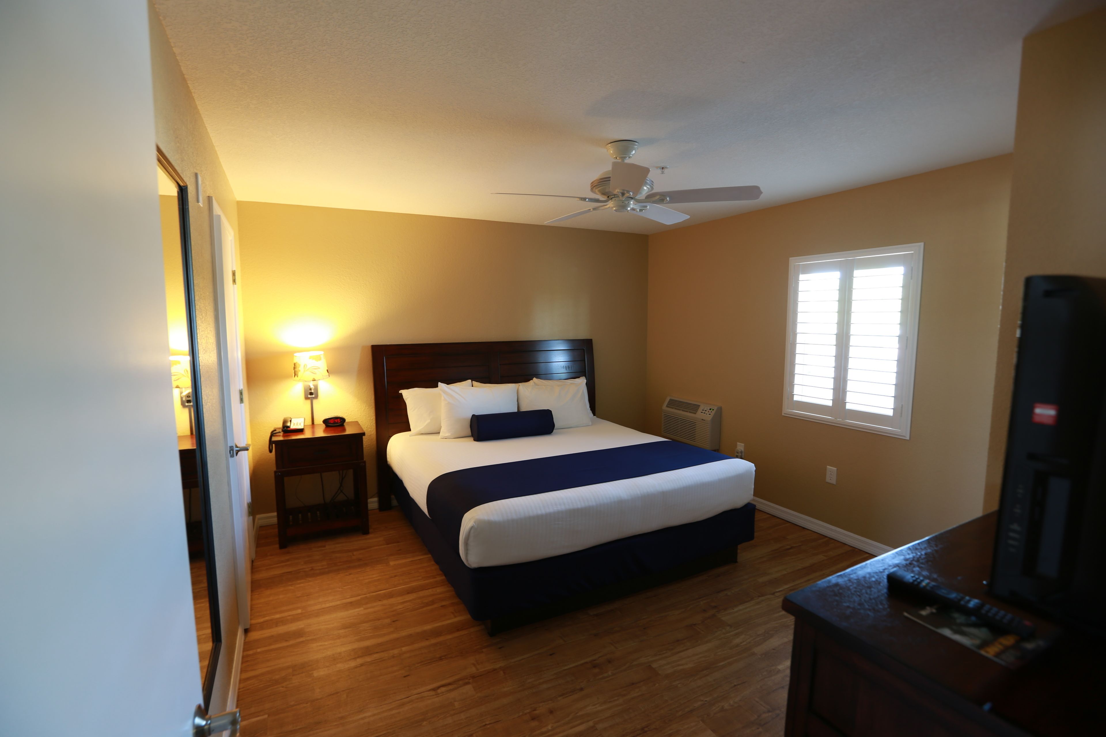 A bedroom with a bed, bedside table, lamp, ceiling fan, and a window.