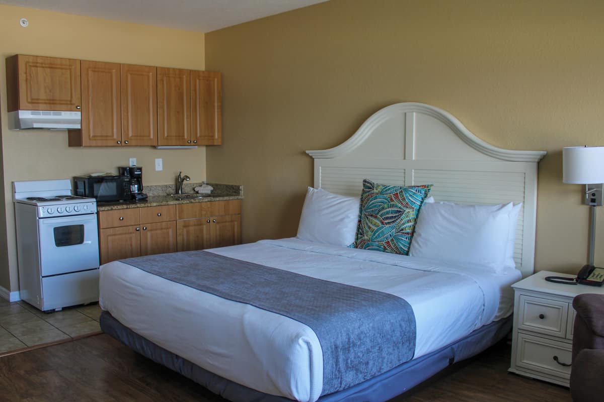Una habitación de hotel con cama, mesita de noche, lámpara, microondas, estufa y armarios de madera.