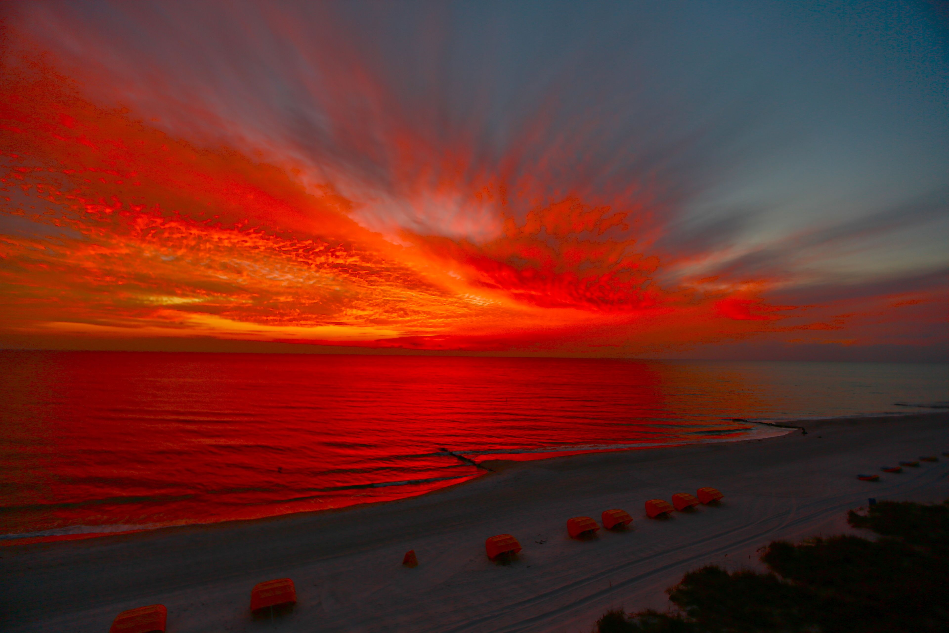 A beach with a sunset, calm sea, and beach umbrellas.