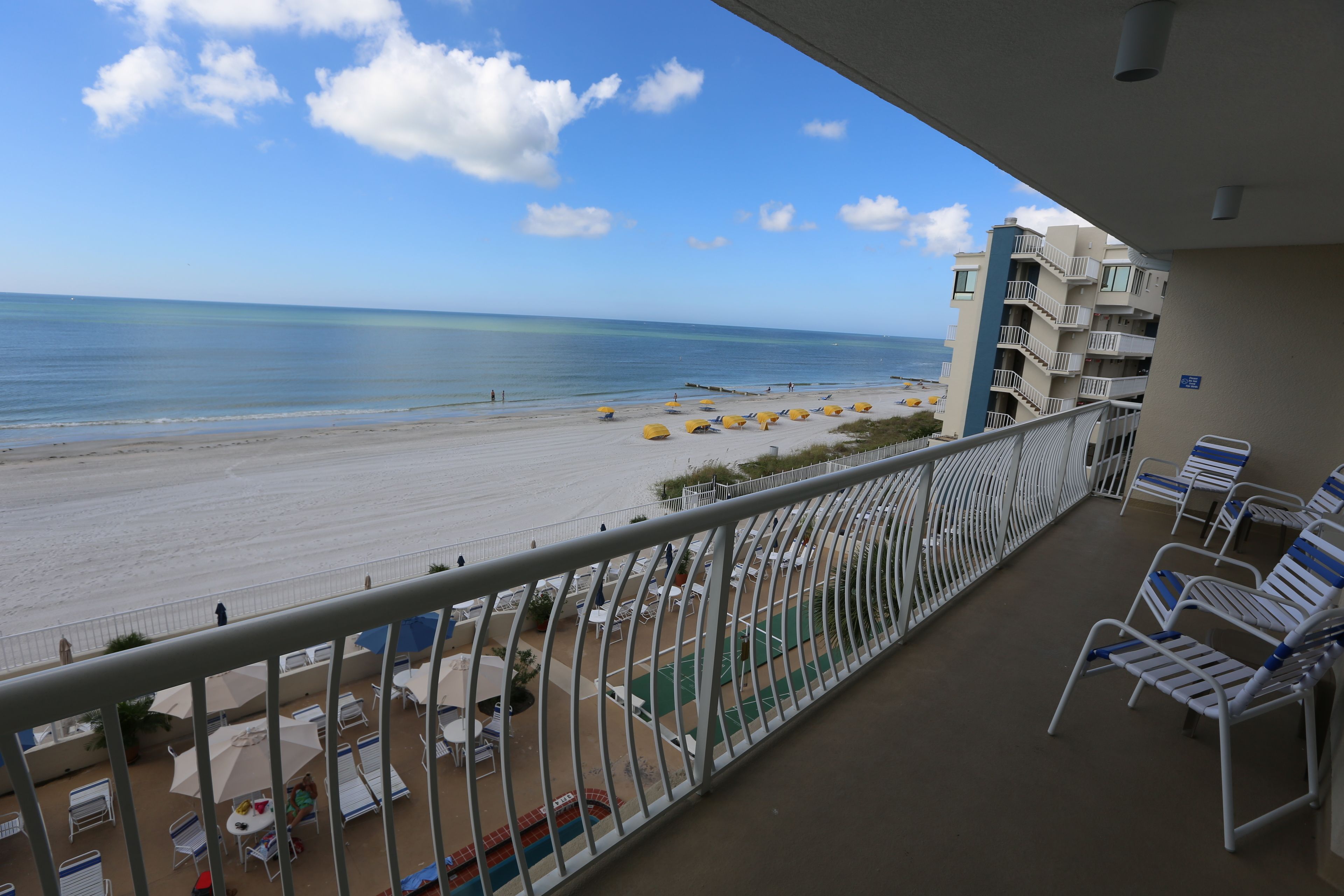 Een balkon met uitzicht op een strand, zitplaatsen buiten en een zwembad.