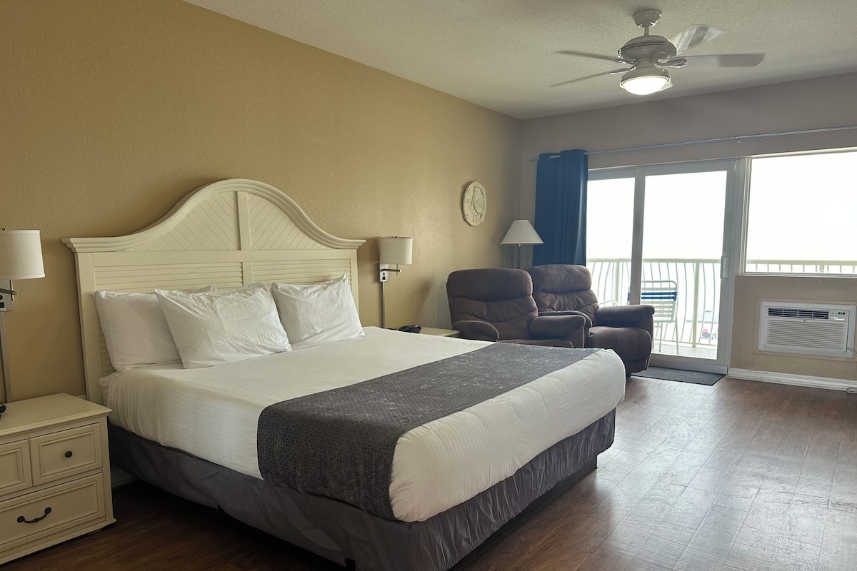 Una habitación de hotel con cama, mesitas de noche, una silla, balcón y ventilador de techo.