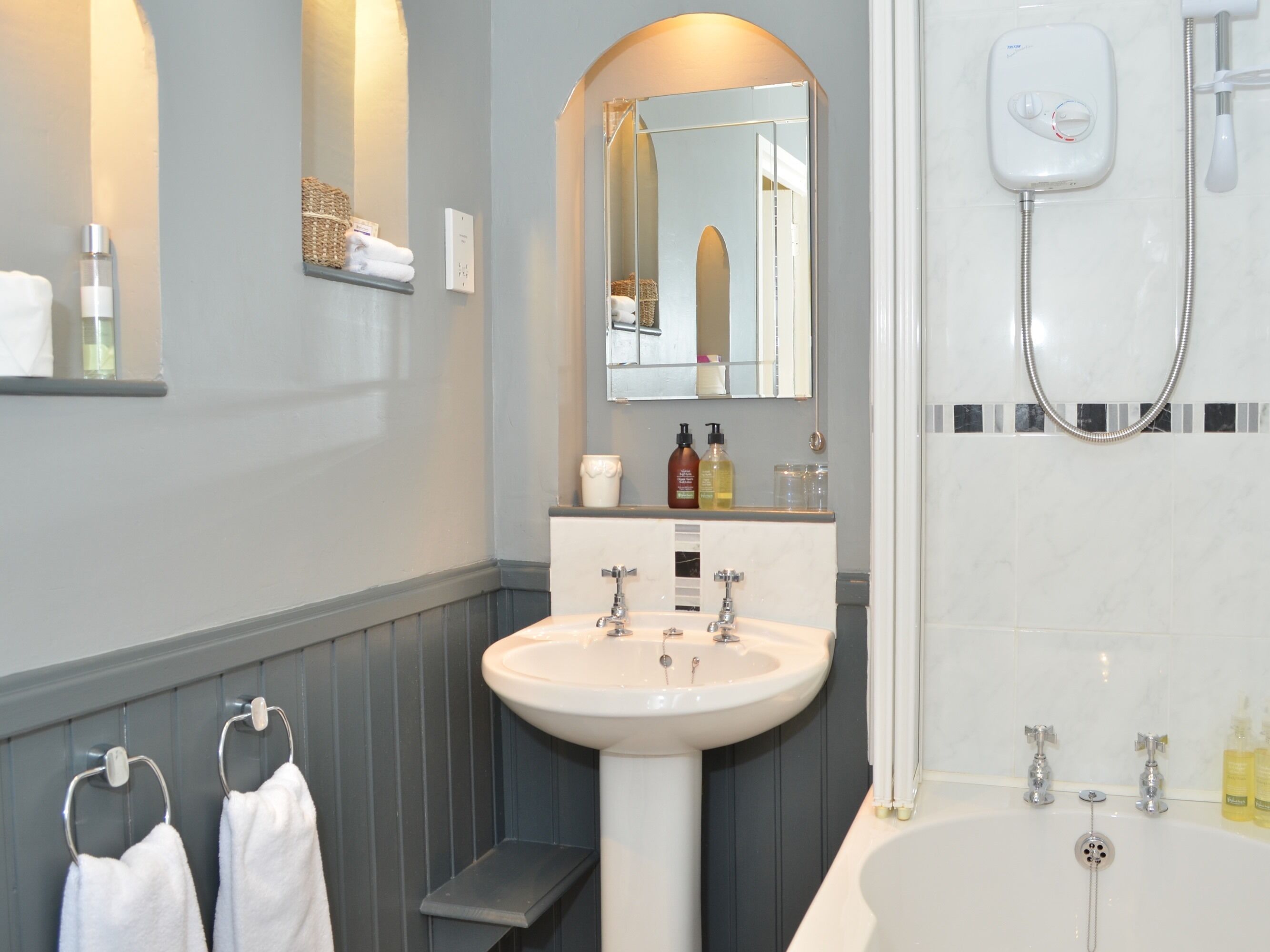 Un bagno con lavandino bianco, specchio e vasca. Asciugamani su uno porta-asciugamani e articoli da toilette sul piano del lavabo.