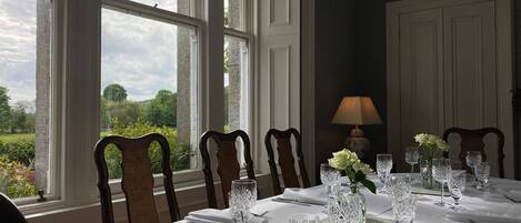 A dining room with a table set for a meal, large windows, and a view of greenery.