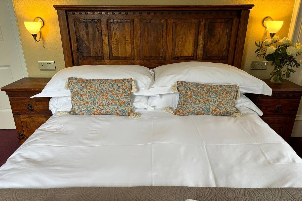 A double bed with white linens and floral-patterned pillows, flanked by wooden nightstands with wall sconces.