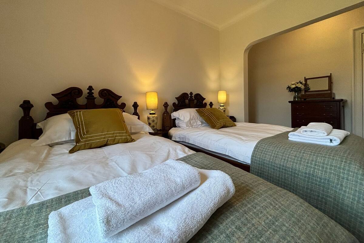 A hotel room with two beds, each with white linens and decorative pillows. There are bedside lamps and a dresser with a mirror.