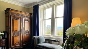 Una habitación con un mueble grande de madera, una silla tapizada de gris, una alfombra azul estampada y una ventana con cortinas.