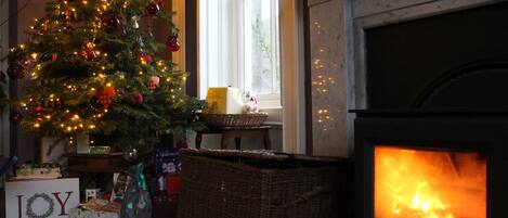 Une pièce chaleureuse avec un sapin de Noël décoré, une cheminée et un panneau indiquant le mot « JOIE ».