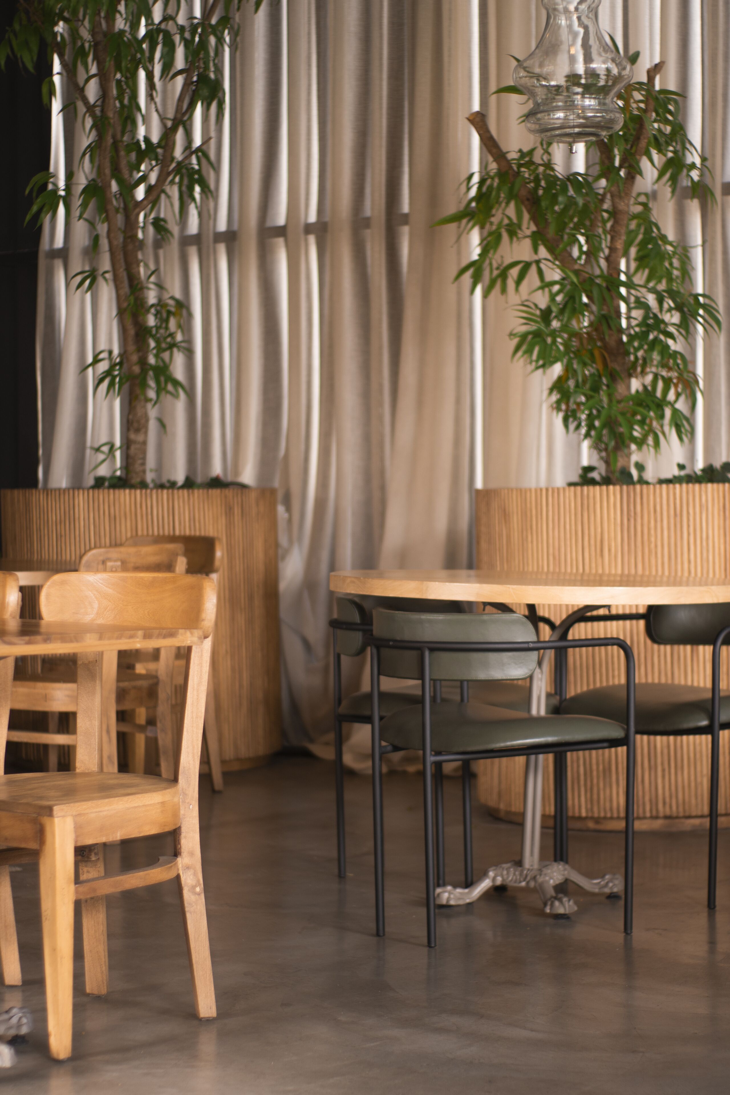 Een eetgedeelte met houten stoelen en een tafel, een bamboe plant en een gordijn als achtergrond.