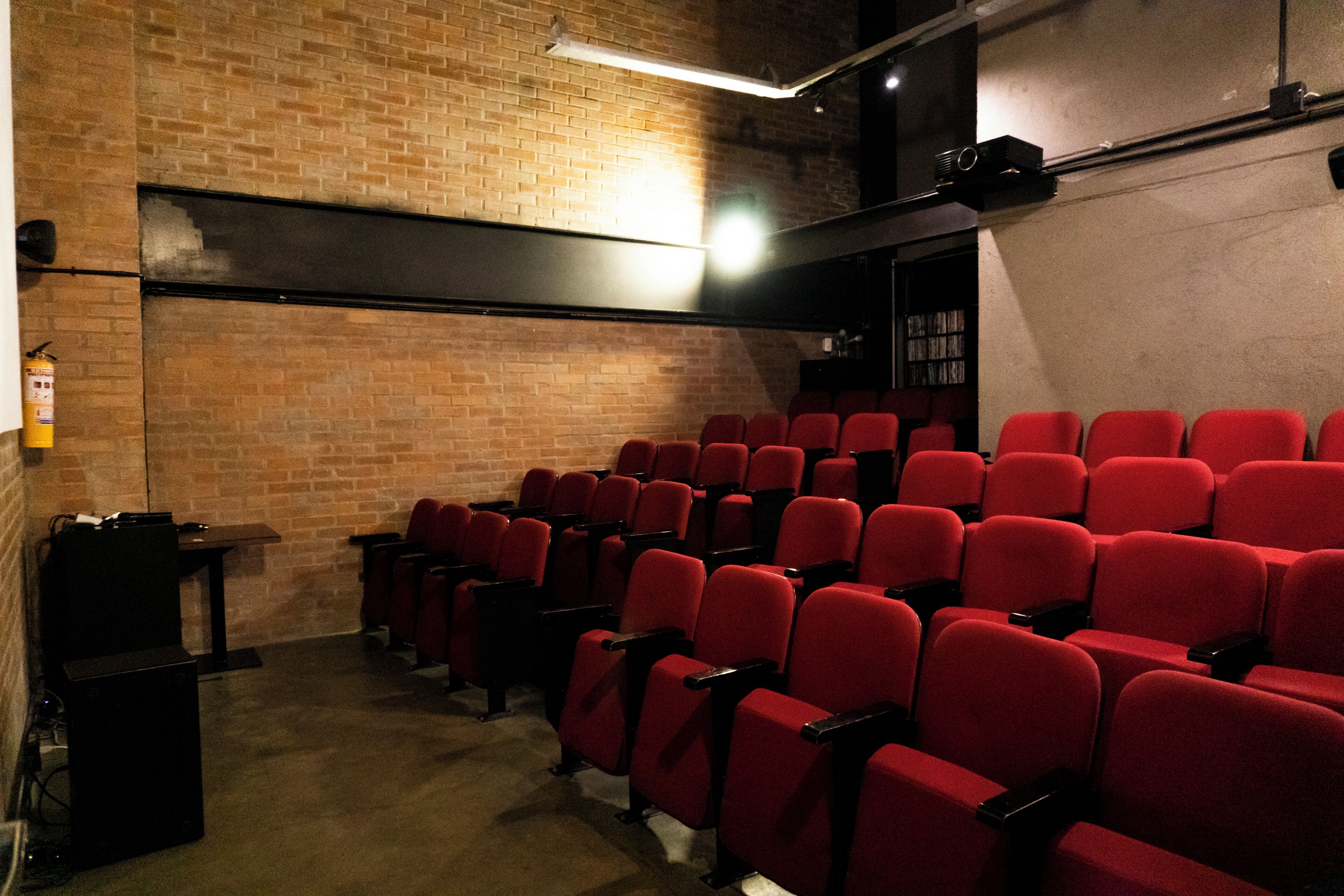 A theater with red seats, a brick wall, and a projector screen.