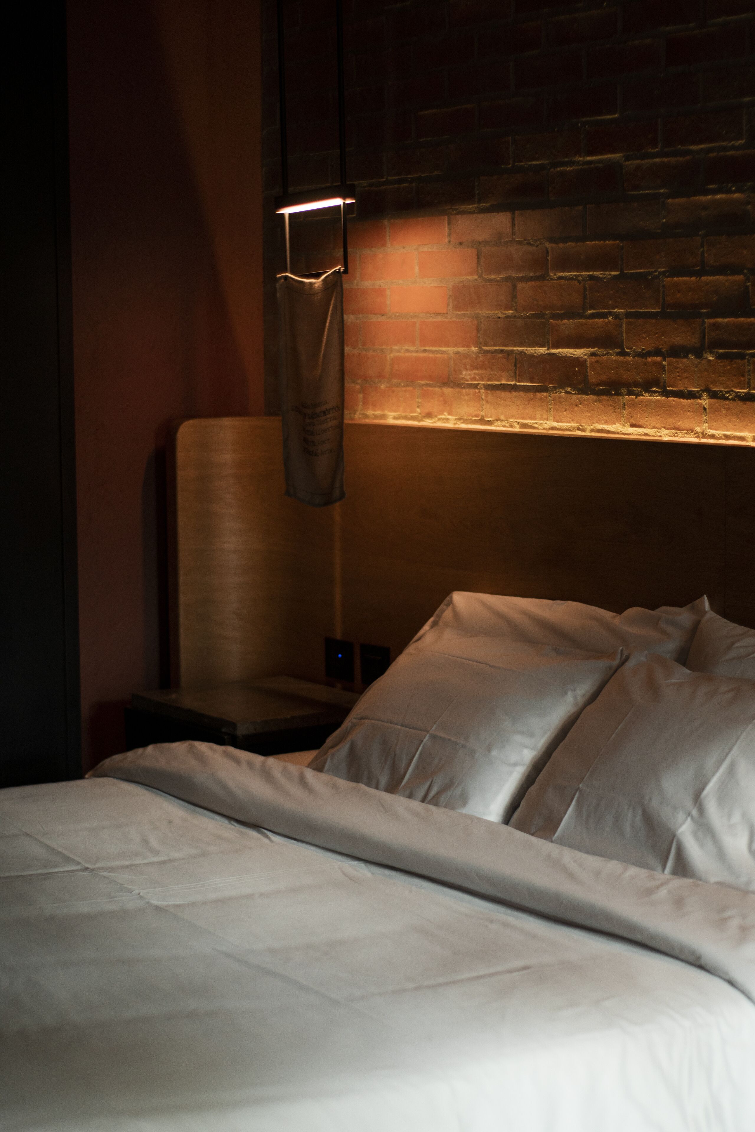 Una cama bien hecha con sábanas blancas en una habitación con pared de ladrillo y una toalla colgada.