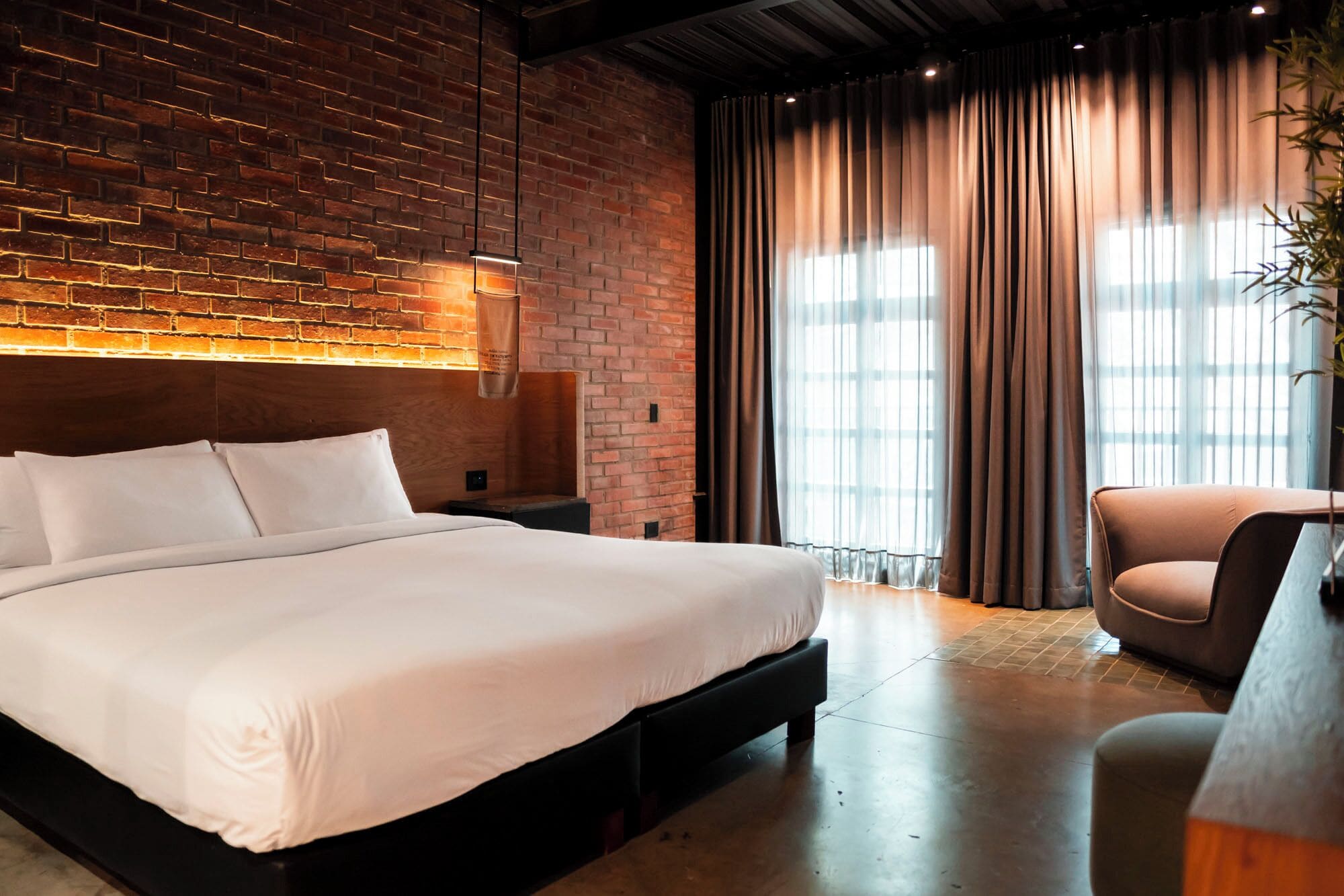 A modern hotel room with a brick wall, a large bed, a desk, and a chair.