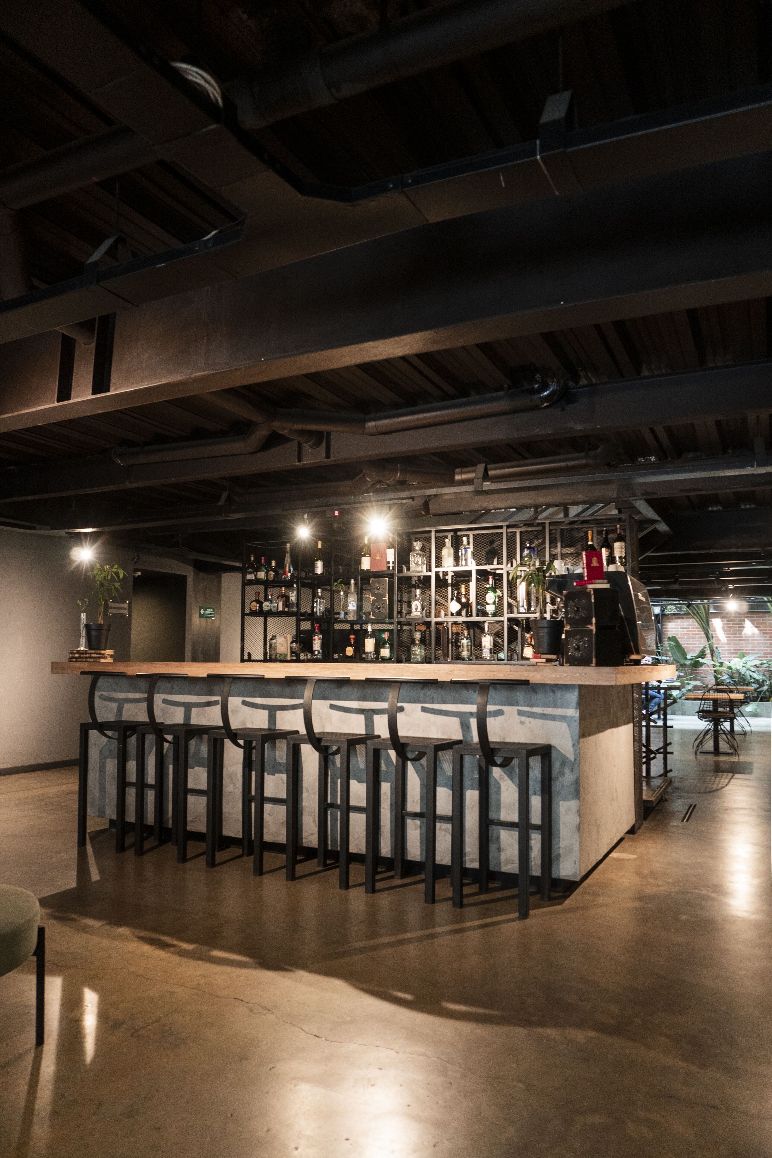 Zona de bar con una barra central, taburetes y estantes llenos de botellas.