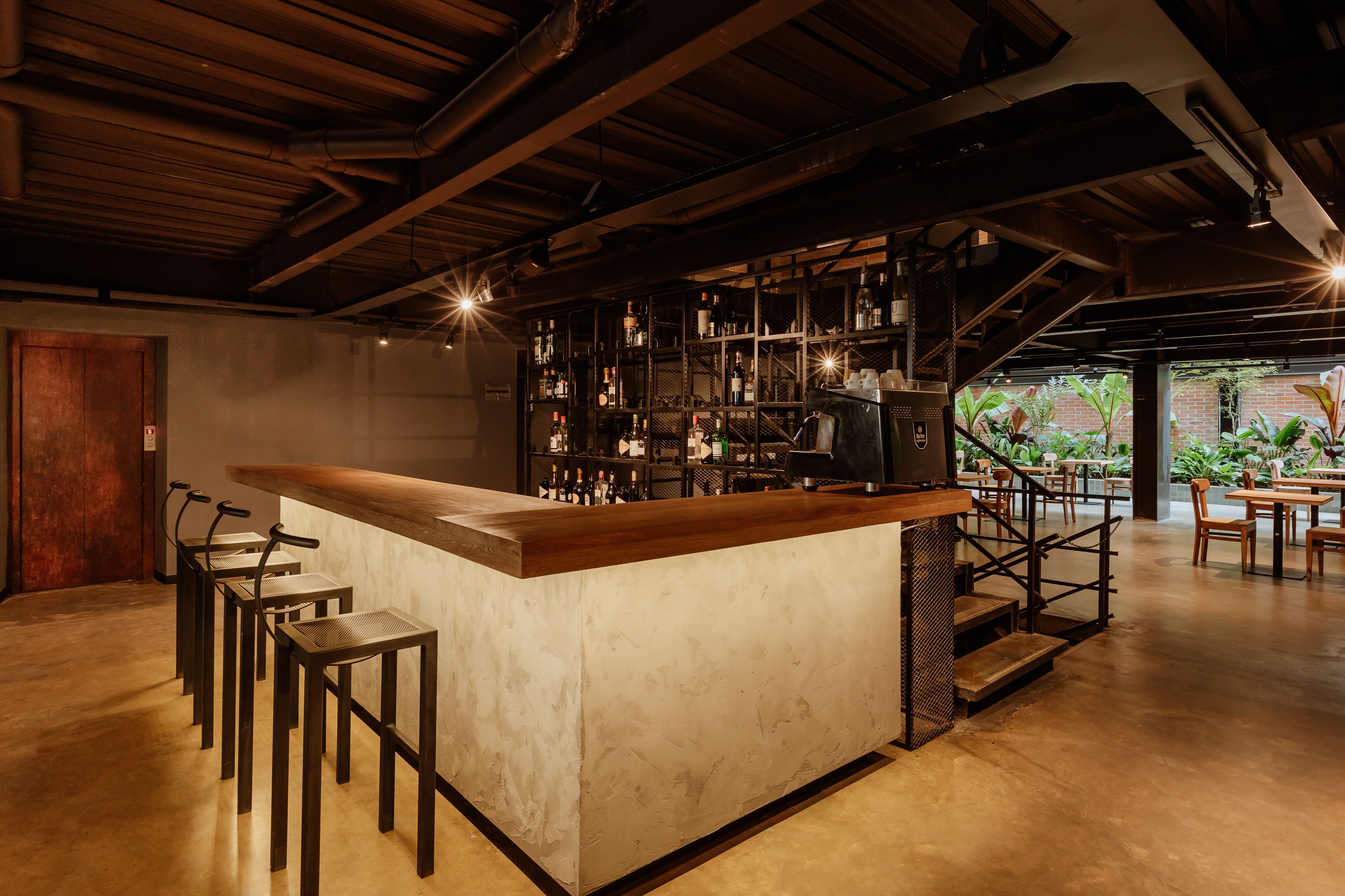 A bar area with a long counter, stools, and a staircase leading to an outdoor seating area.