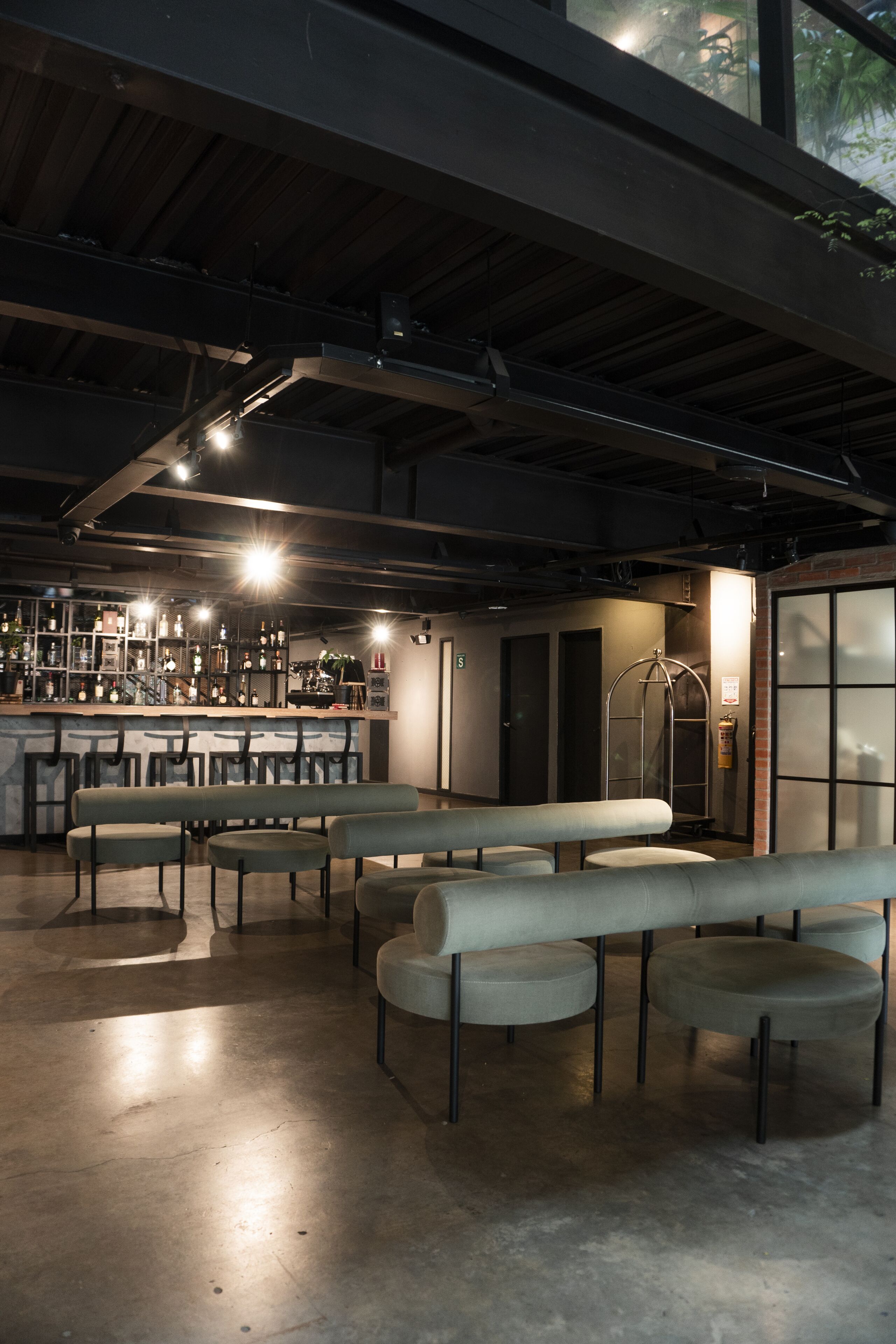 A spacious bar area with multiple seating options, including benches and high tables, and a visible bar counter with bottles and glasses.
