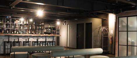 A spacious bar area with multiple seating options, including benches and high tables, and a visible bar counter with bottles and glasses.