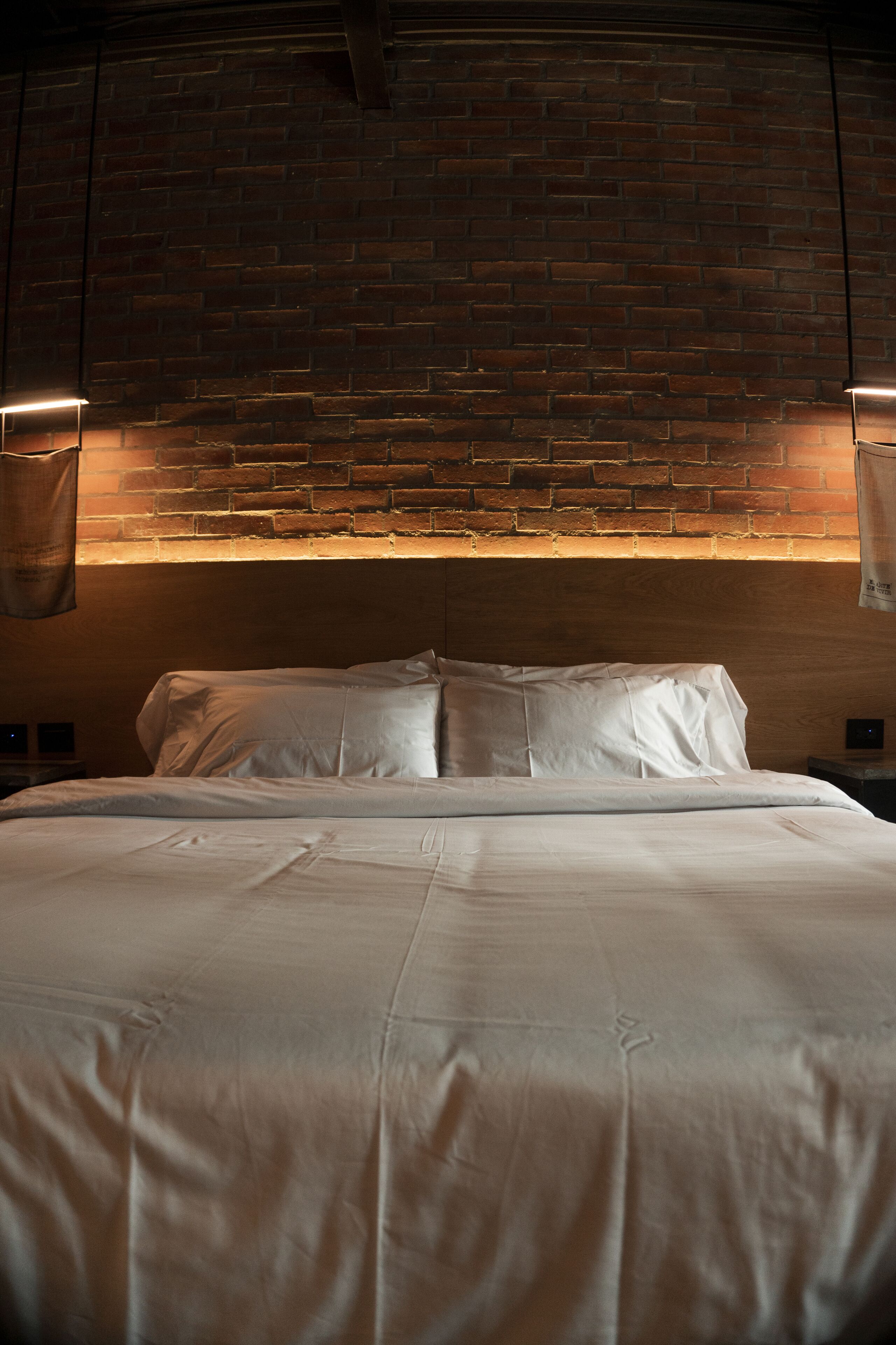 A neatly made bed in a room with a brick wall and two wall-mounted lamps.