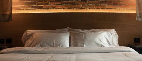 A neatly made bed in a room with a brick wall and two wall-mounted lamps.